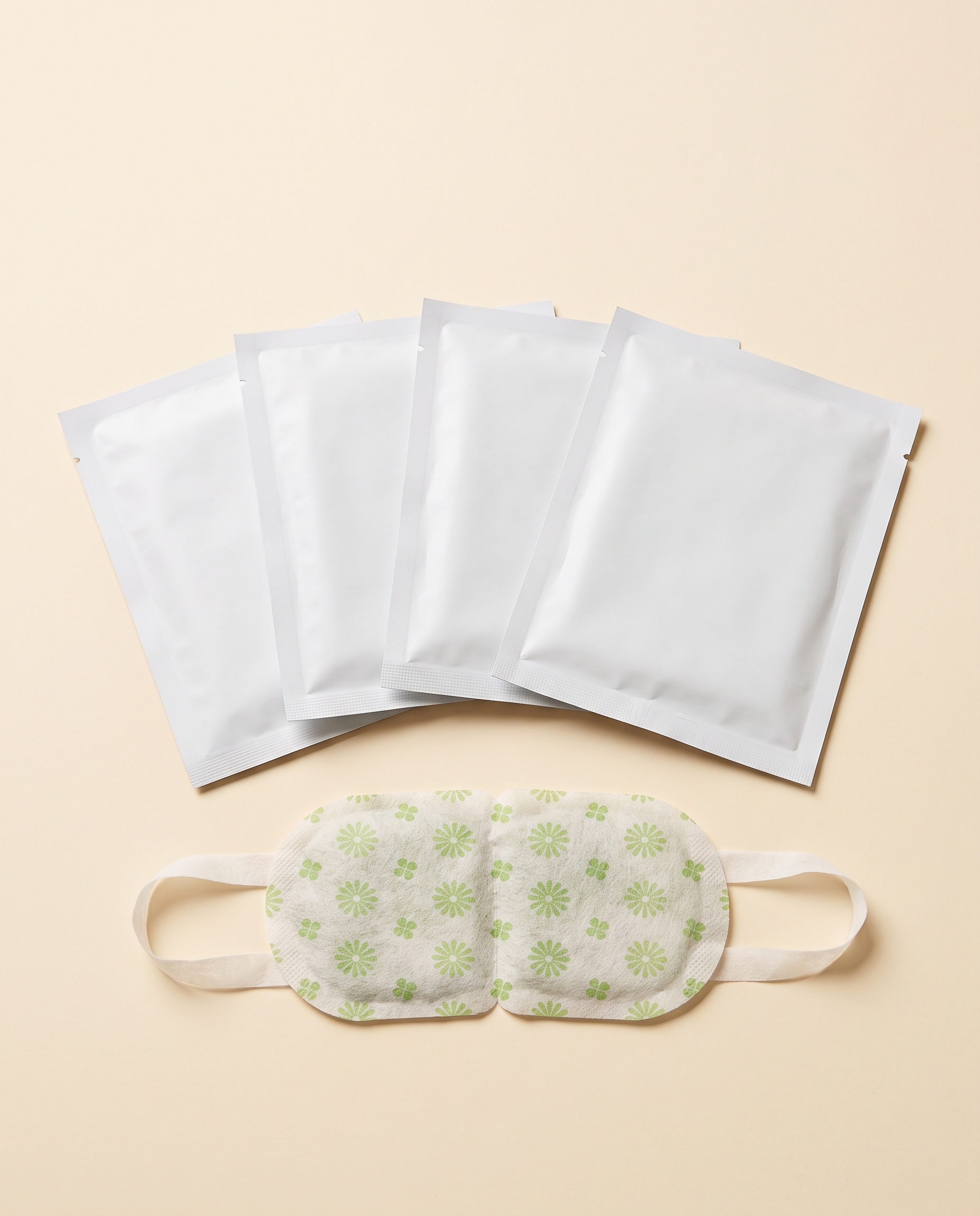 Five self-warming eye masks: four sealed pouches and one unfolded mask with green floral print